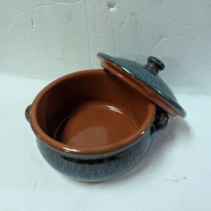 May include: A ceramic casserole dish with a lid. The dish is a deep brown color on the inside and has a dark blue exterior with a speckled pattern. The lid is also dark blue with a small handle.
