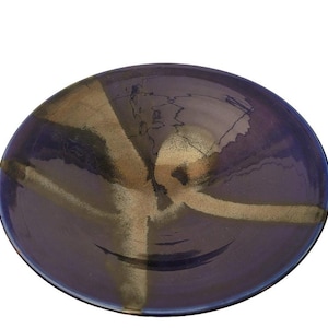 May include: A round, ceramic bowl with a dark blue exterior and a gold-colored, cross-shaped design. The bowl's interior has a glossy finish, and the gold design appears to be painted on. The bowl is likely used for serving food or as a decorative piece.