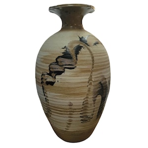 May include: A ceramic vase with a tapered neck and a flared rim, featuring a cream-colored base with horizontal brown striations and a prominent, dark, wavy, textured pattern that sweeps across the body in a vertical, organic design.