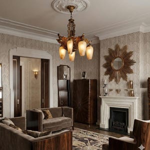 May include: An interior shot of a living room with Art Deco style furniture. A gold chandelier hangs from the ceiling. There is a brown sofa, a fireplace, and a sunburst mirror. The walls are covered in patterned wallpaper.