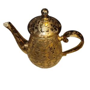 May include: A metallic gold teapot featuring a mottled, textured surface pattern throughout the body, lid, and handle. The teapot includes a curved spout, a rounded lid with a small knob handle, and a C-shaped handle on the side.