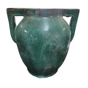 May include: A green ceramic vase with two square handles. The vase has a textured surface and a rounded body. The color is a deep, mottled green with hints of brown at the rim. The vase is likely for decorative use.