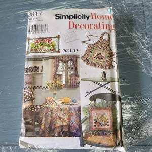 May include: A Simplicity Home Decorating sewing pattern envelope, number 9817, featuring Mary Engelbreit designs. The package displays illustrations of a floral apron, a table setting with a patterned tablecloth, curtains, and a decorative pillow.