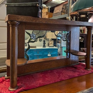 May include: A dark wood bar with a mirrored back and decorative floral accents. The bar has two small shelves and is supported by four rounded columns. A red rug is at the base of the bar. The word "TIX" is visible on the mirror.