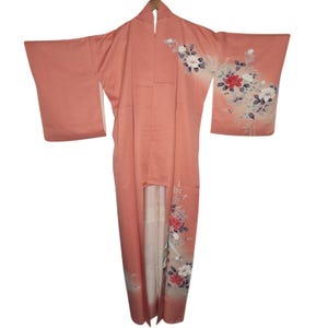 May include: A coral-colored kimono with floral embroidery. The long-sleeved garment features a vertical design with white, red, and gray flowers. The kimono is open in the front, revealing a cream-colored lining.