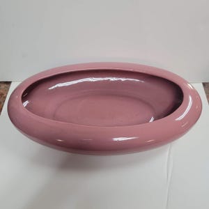 May include: A dusty rose-colored, oval-shaped ceramic planter. The planter has a smooth, glossy finish and a wide, open top. The interior is the same color as the exterior.