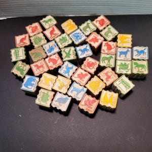 May include: A collection of small, square wooden blocks featuring various colorful illustrations of animals, objects, and text labels. Each block displays a unique graphic in red, blue, green, or yellow ink, depicting subjects like a wolf, zebra, horse, and xylophone.