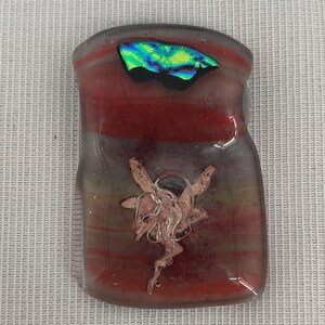 May include: A rectangular glass pendant with a layered design of red, gray, and green hues. The pendant features a dichroic glass accent with iridescent colors and a copper-colored, stylized floral design.