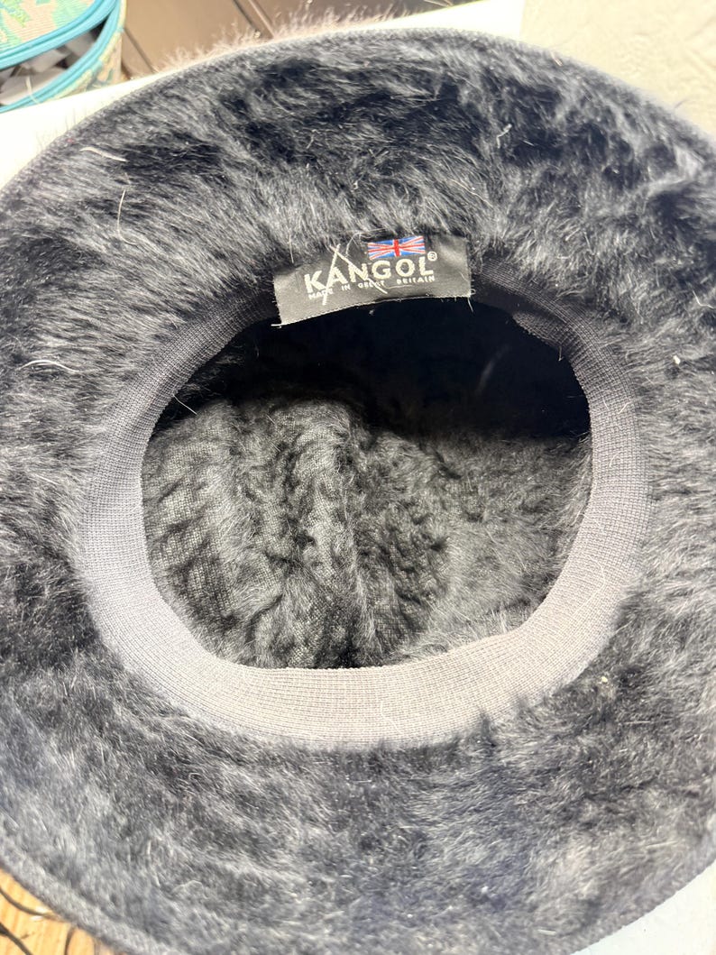 K&ouml;nnte beinhalten: Eine wei&szlig;e Keramik-Tasse mit schwarzem Henkel und dem Text "But First, Coffee" in schwarzer, handschriftlicher Schrift. Die Tasse steht auf einer wei&szlig;en Oberfl&auml;che.