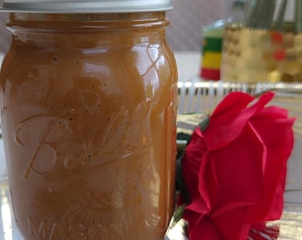 May include: A glass jar filled with a brown substance, possibly a preserve or sauce, with a silver lid. A red rose lies beside the jar on a decorative surface. The jar is embossed with the word "Ball" and "MASON".