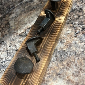 Peut inclure: Une planche en bois avec quatre crochets en métal noir. Les crochets sont fabriqués à partir de pointes de chemin de fer réutilisées. La planche est teintée d'une couleur brun foncé et a une finition vieillie.