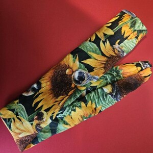 May include: Two oven mitts with a sunflower pattern on a black background. The mitts feature yellow sunflowers, green leaves, and a red background.