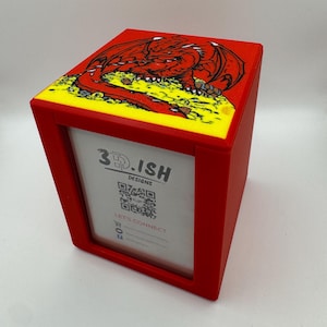 May include: A red rectangular display stand featuring a top panel with a graphic of a red dragon resting on a pile of yellow gold. The front face displays a white card with the text 3D.ISH DESIGNS, a QR code, and the phrase LET'S CONNECT.
