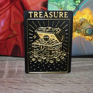 May include: A black card with gold lettering that says "TREASURE". The card features a gold illustration of a treasure chest overflowing with gold coins and a large diamond.