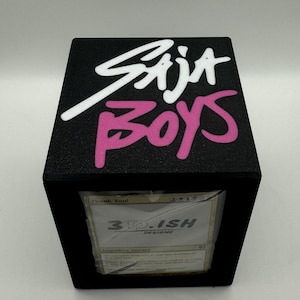 May include: Black cube-shaped box with the words "Saja Boys" in white and pink lettering on top. The box has a clear front panel displaying a card with the text "Thank You!" and "3D-ISH DESIGNS".