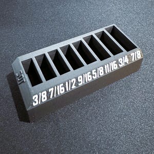 Pode incluir: Um organizador de plástico preto com oito compartimentos para guardar ferramentas. Os compartimentos são etiquetados com os seguintes tamanhos: 3/8, 7/16, 1/2, 9/16, 5/8, 11/16, 3/4, 7/8.