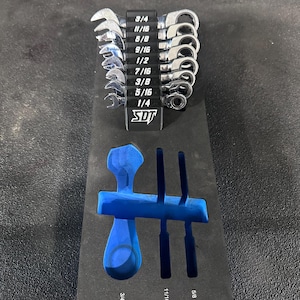 Może przedstawiać: Czarny organizer na narzędzia z pianki z niebieską wkładką. Organizer zawiera zestaw 10 kluczy nasadowych z grzechotką z zaznaczonymi rozmiarami po bokach: 5/16, 3/8, 7/16, 1/2, 9/16, 5/8, 11/16, 3/4, 7/8 i 1. Organizer ma również gniazda na trzy większe klucze, oznaczone jako 5/8, 11/16 i 3/4.