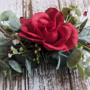 May include: A red rose with green leaves and silver stems with red beads, attached to a silver comb.