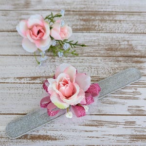 May include: Two floral arrangements. One is a cluster of pink and white roses with greenery. The other is a silver nail file adorned with a large pink rose, pink glitter ribbon, and white tulle.