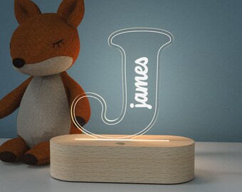 May include: A wooden night light with a clear acrylic letter J that has the name "james" written inside. The light is on and illuminating the letter.