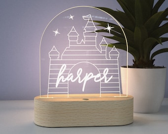Puede incluir: Una luz nocturna de madera blanca con forma de castillo con el nombre "harper" escrito debajo. El castillo tiene un techo puntiagudo y una bandera en la parte superior. Hay tres estrellas en el fondo.