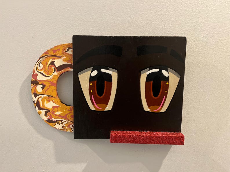 May include: A quirky wall decoration depicting a face with large, cartoon-like eyes. The eyes are brown with pink details, set against a black backdrop. A red, glittery shelf is below the eyes, and a circular handle with a marbled design is on the left.