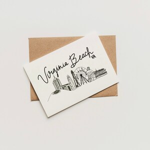 May include: A white card with a black and white illustration of the Virginia Beach skyline, including a Ferris wheel. The text "Virginia Beach VA" is written in cursive above the illustration.