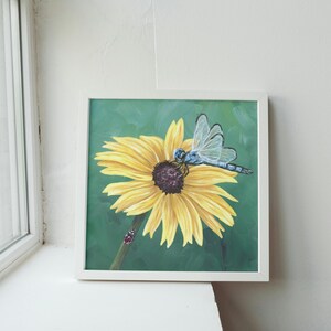 May include: A framed painting of a blue dragonfly perched on a yellow sunflower with a green background.