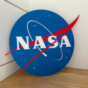May include: A blue and red NASA logo with a white background. The logo is a circle with a red curved line and a white NASA text.