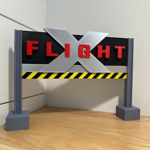 May include: A black and silver sign with the word "FLIGHT" in red letters. The sign is mounted on two gray posts with black and yellow striped barriers.