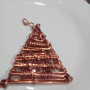 May include: A copper wire triangle pendant with a detailed, intricate design. The pendant has a loop at the top for hanging.