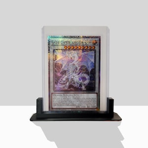 May include: A clear plastic case with a black base holds a "Blue-Eyes Spirit Dragon" trading card. The card features a white dragon with blue wings and a holographic background. The card text reads "DRAGON/SYNCHRO/EFFECT] Tuner - non-Tuner "Blue-Eyes" monsters Neither player can Special Summon more than one monster at the same time. Once per turn, when a card in the Graveyard is activated by a card effect, you can negate the activation and destroy that card. If this card is Synchro Summoned, Special Summon 1 "Blue-Eyes Spirit Dragon" from your Deck. You can only use this effect of "Blue-Eyes Spirit Dragon" once per turn. ATK/2500 DEF/3000 59627133 1st Edition"