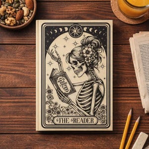 May include: A beige journal with a black and white illustration of a skeleton reading a book. The book reads "How to Read 2 Books at the Same Time." The journal is framed with a decorative border and the words "The Reader".