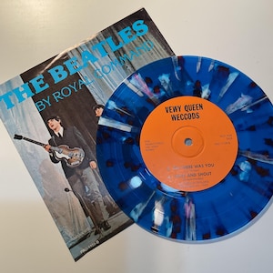 May include: A vinyl record and album cover of The Beatles. The record is blue with a speckled pattern and an orange label. The album cover features a band photo and the words "THE BEATLES BY ROYAL COMMAND".