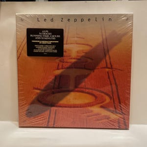 May include: A sealed Led Zeppelin album with a warm, orange-toned cover featuring an abstract design. The album cover includes text indicating 6 LPs, 54 tracks, and a running time of 4 hours and 50 minutes. The album is digitally remastered.