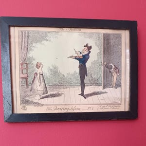 May include: A framed antique print titled "The Dancing Lesson Pt. 1". The cartoon depicts a man in a blue coat playing a violin, a girl in a dress, and a man peeking through a door. The frame is black.