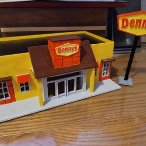 May include: A yellow and brown model of a Denny's restaurant with a red and yellow sign that reads "Denny's".