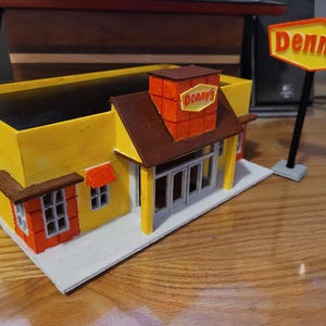 May include: A yellow and brown model of a Denny's restaurant with a red roof and a sign that says "Denny's".