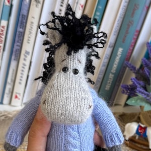 May include: Handmade knitted horse doll with a gray and white head, black mane, and blue sweater and pants. The doll has yellow and blue striped socks. A charming, whimsical toy.