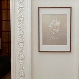 May include: A framed print with a white anatomical heart illustration and the word "Chaos" written below it. The print is on a beige background and has a brown frame.