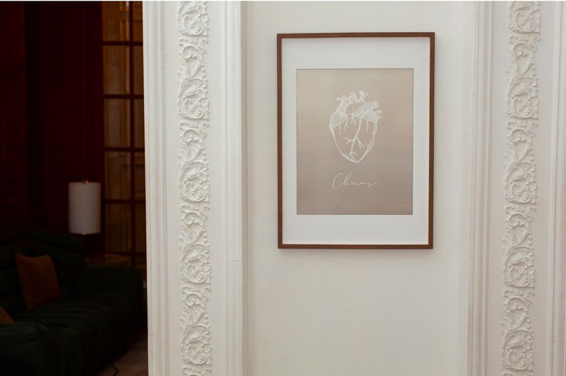 May include: A framed print with a white anatomical heart illustration and the word "Chaos" written below it. The print is on a beige background and has a brown frame.
