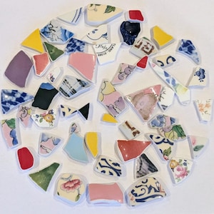May include: A circular arrangement of broken ceramic shards. The fragments are in diverse shapes and sizes, featuring a variety of colours such as blue, yellow, pink, and green, with floral and geometric designs. Some pieces have text.