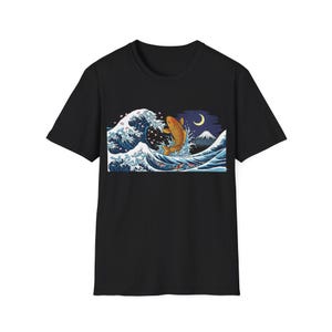 May include: Black t-shirt featuring a graphic of a golden koi fish leaping over a large ocean wave. The design includes a crescent moon, Mount Fuji, and cherry blossoms, inspired by Japanese art.