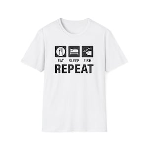 Puede incluir: Camiseta blanca con un diseño gráfico negro. El diseño incluye iconos de comer, dormir y pescar, con la palabra "REPEAT" debajo. Una camiseta informal para los amantes de la pesca.