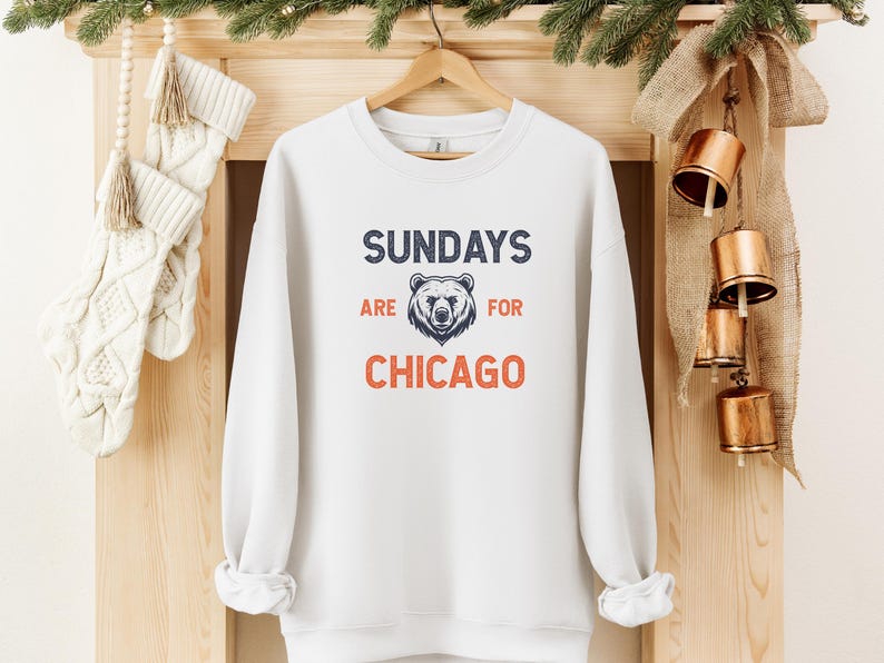 K&ouml;nnte beinhalten: Wei&szlig;er Pullover mit dem Text "Sundays are for Chicago" in Marineblau und Orange. Eine B&auml;renkopfgrafik befindet sich in der Mitte des Textes.