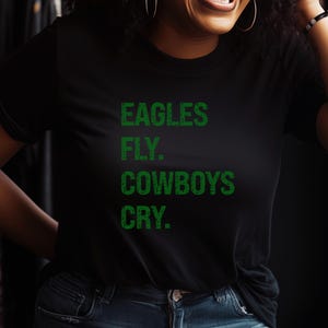 May include: Black t-shirt with the text "EAGLES FLY. COWBOYS CRY." in green block letters. The shirt is a classic crew neck style.
