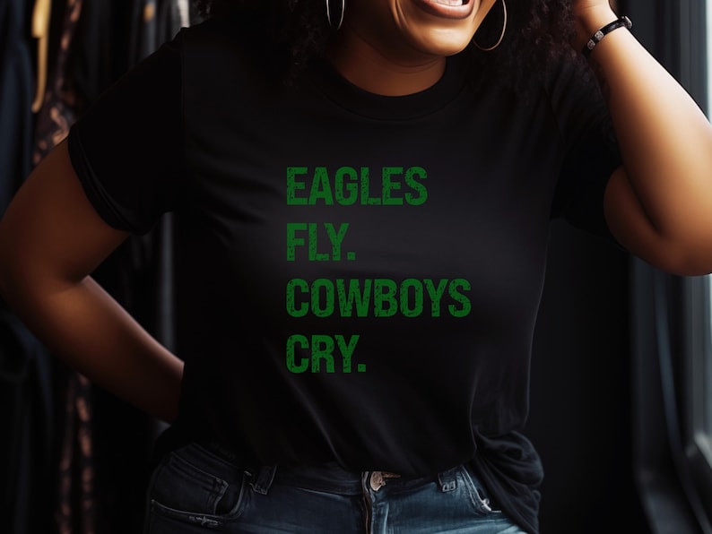 May include: Black t-shirt with the text "EAGLES FLY. COWBOYS CRY." in green block letters. The shirt is a classic crew neck style.