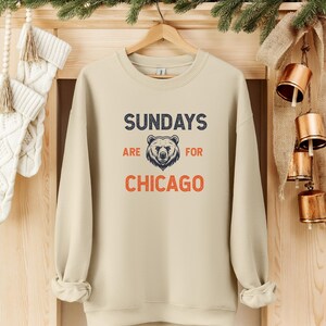 K&ouml;nnte beinhalten: Ein beiger Pullover mit dem Aufdruck "SUNDAYS ARE FOR CHICAGO" auf der Vorderseite. Ein B&auml;renkopf befindet sich in der Mitte des Textes.