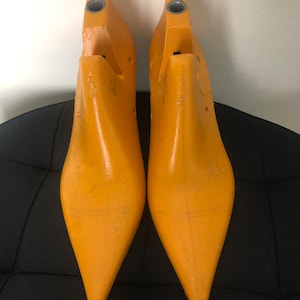 Puede incluir: Un par de hormas de zapatos de plástico amarillo con puntas puntiagudas. Las hormas se utilizan para dar forma a los zapatos.
