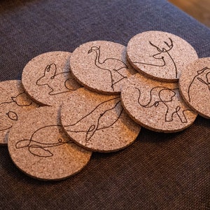 May include: A set of eight cork coasters featuring various animal designs, including a flamingo, deer, elephant, whale, and dog. The coasters are round and have a natural cork finish.